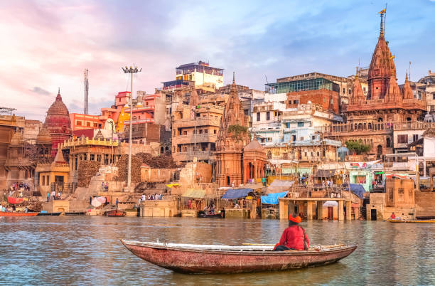 Ancient Varanasi city architecture and Ganges river ghat at sunset with a view of an Indian sadhu sitting on a boat on the river Ganges.
